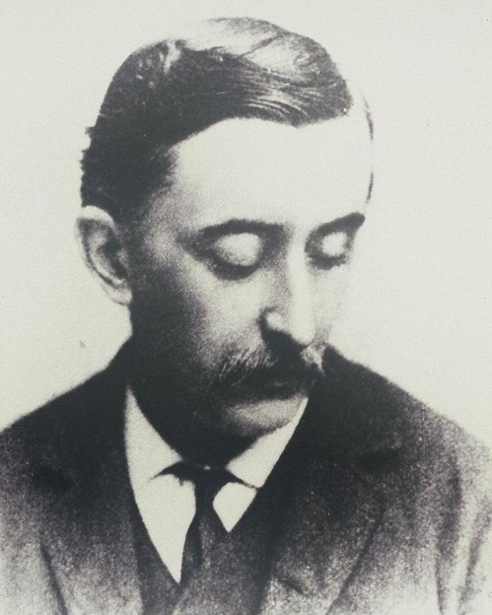 Lafcadio Hearn in profile, looking down, with a dark moustache, a wing collar and a dark coat