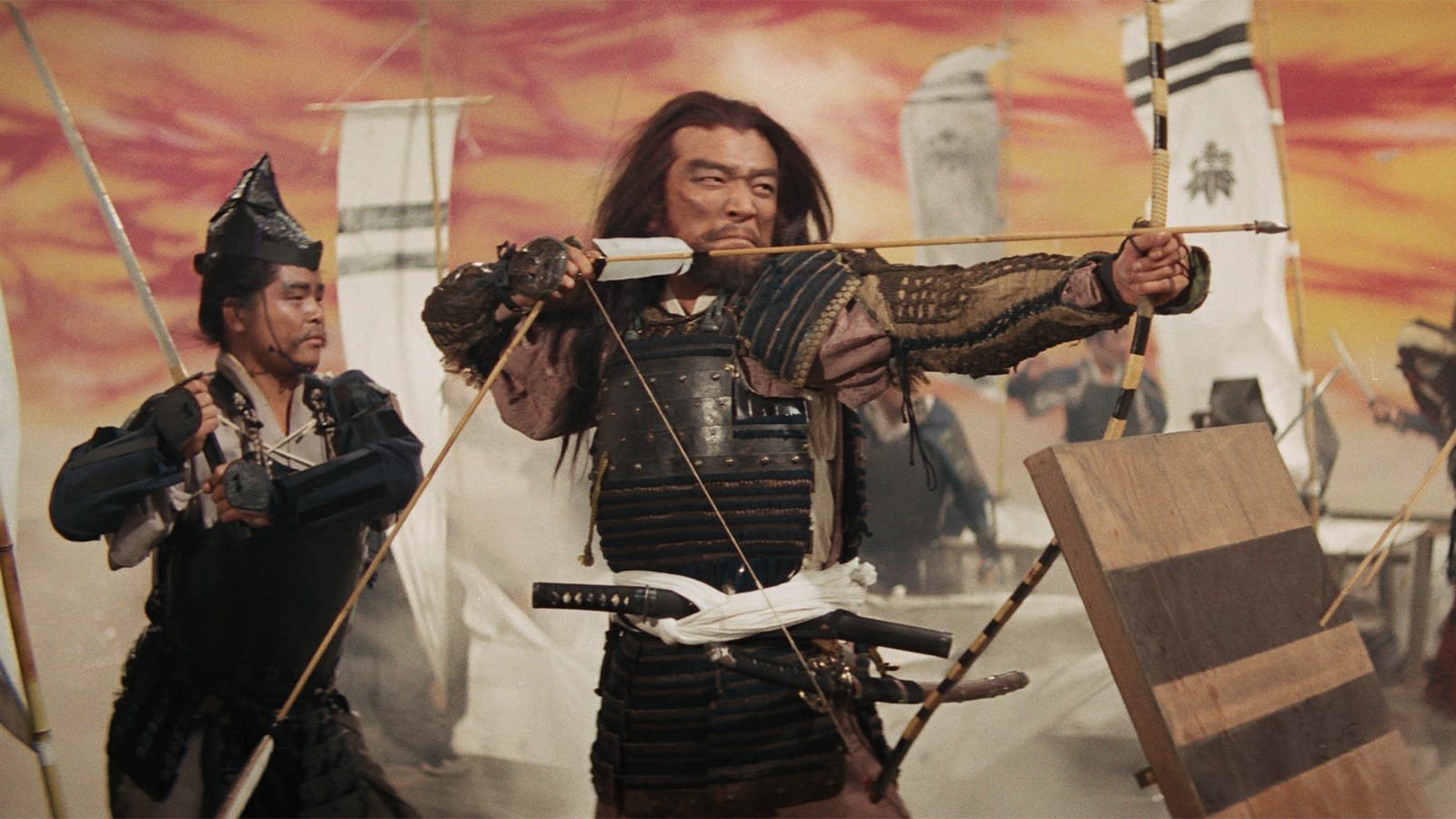 An armored archer with long hair draws a bow beside another warrior, banners and a red painted sky behind them