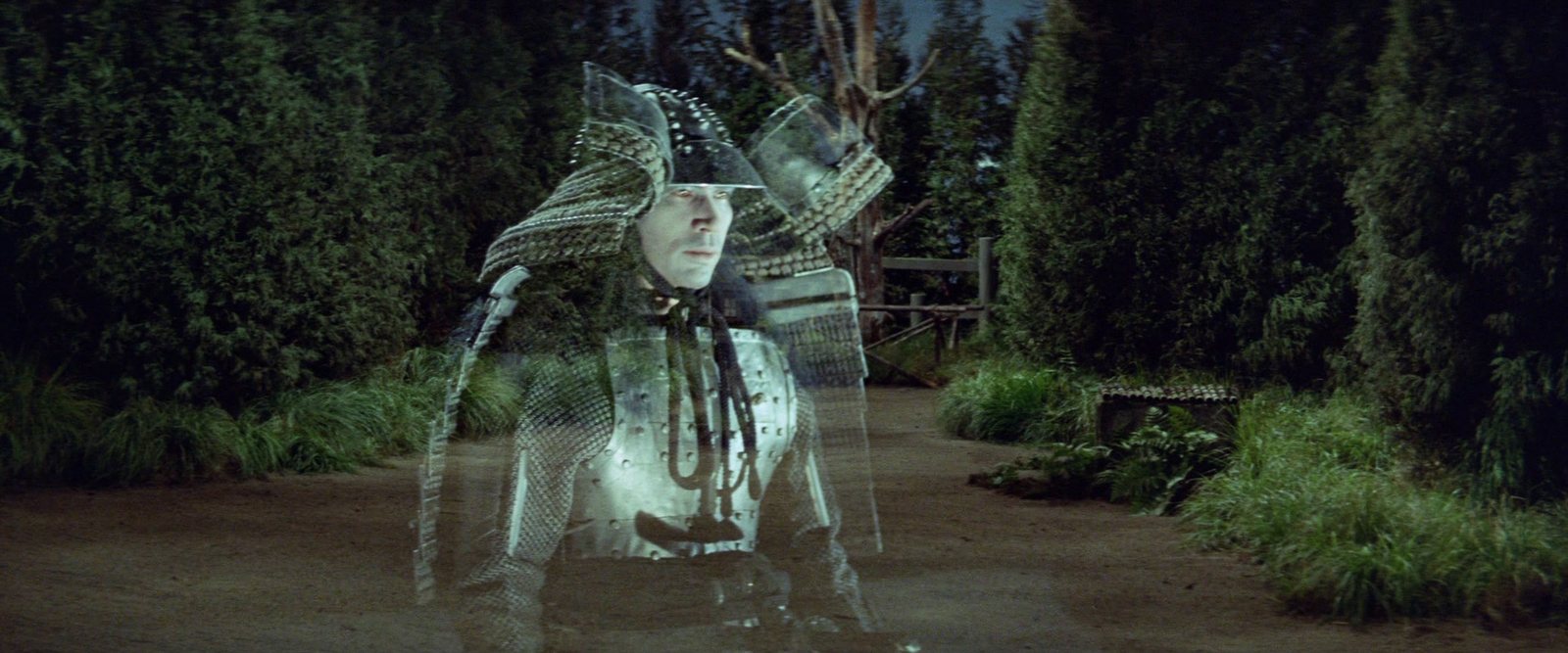 A translucent armored samurai, his face pale, stands on a forest path at night like a figure seen through glass