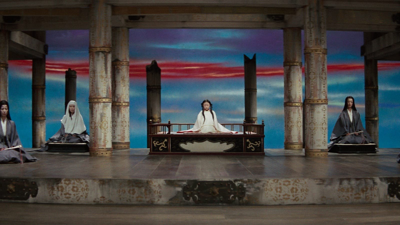 A hall open to a painted sky of red and blue streaks: a child in white sits on a raised dais at the center, a woman in a white hood and court ladies seated to either side
