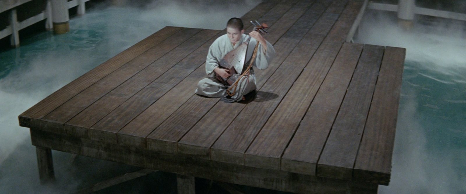 A blind musician sits alone on a square wooden platform floating on a sea of mist, holding his biwa