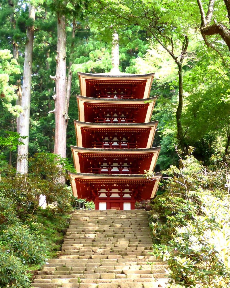 A five-storied pagoda painted red, at the top of a long flight of stone steps in a forest of tall cedars