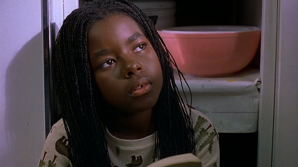 A young girl with long braids looks up from the book in her hands