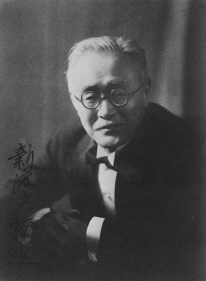 Nitobe Inazō in later life, white-haired, in round spectacles and a dark suit, with his signature written across the photograph