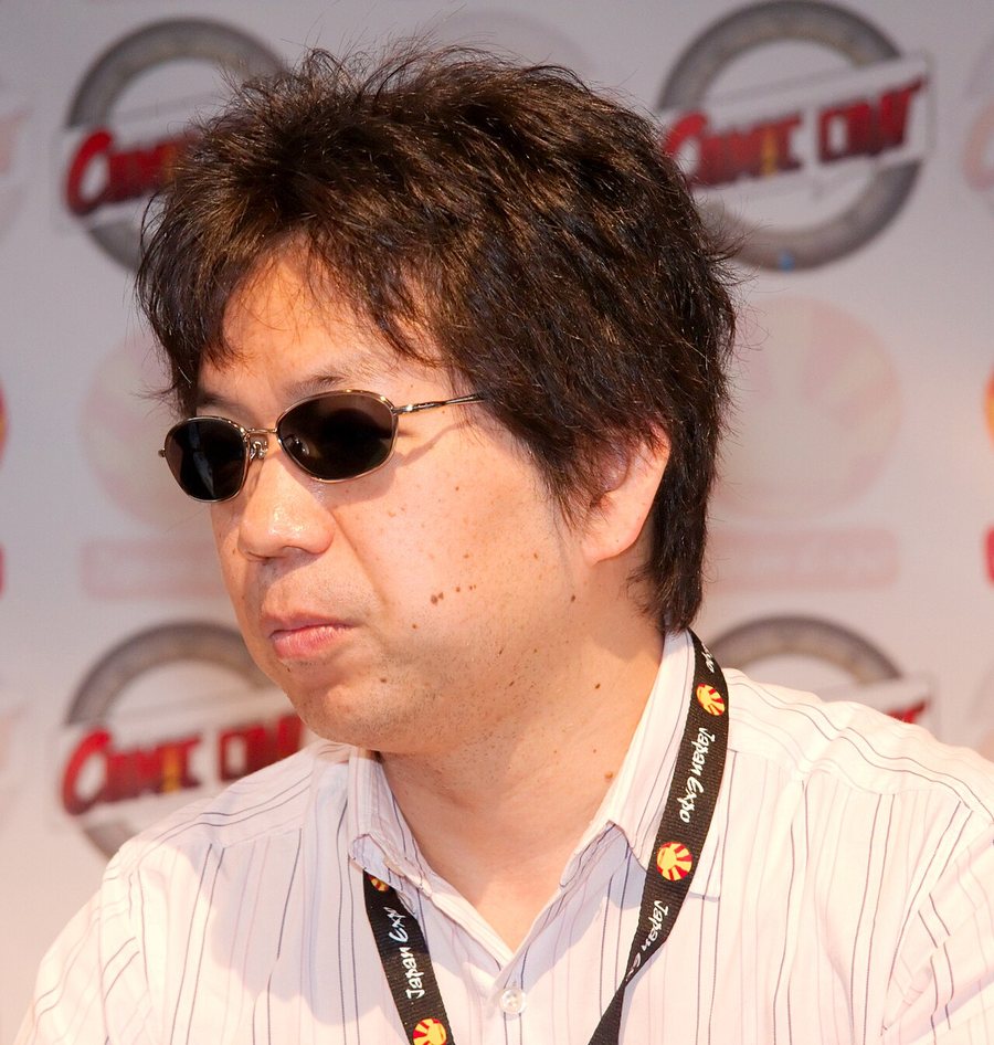Shinichirō Watanabe in dark glasses and a striped shirt, with a convention badge around his neck