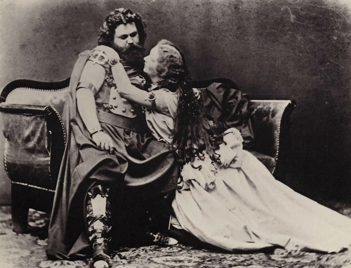 Ludwig and Malvina Schnorr von Carolsfeld in costume as Tristan and Isolde: he leans back on a couch in tunic and boots while she kneels beside him, her long hair loose, her face turned up toward his